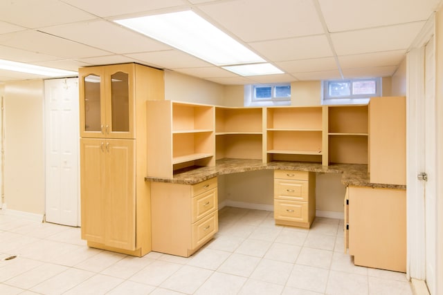 unfurnished office with built in desk, light tile patterned floors, baseboards, and a paneled ceiling