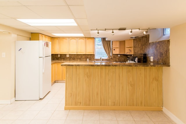kitchen with a sink, a peninsula, freestanding refrigerator, backsplash, and light brown cabinetry