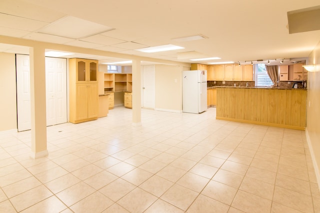 below grade area featuring freestanding refrigerator, rail lighting, and light tile patterned floors