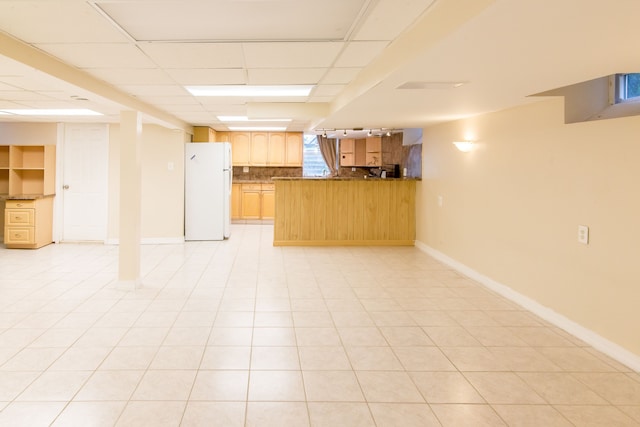 below grade area with freestanding refrigerator, baseboards, and a drop ceiling