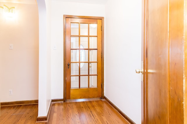 doorway to outside featuring arched walkways, baseboards, and wood finished floors