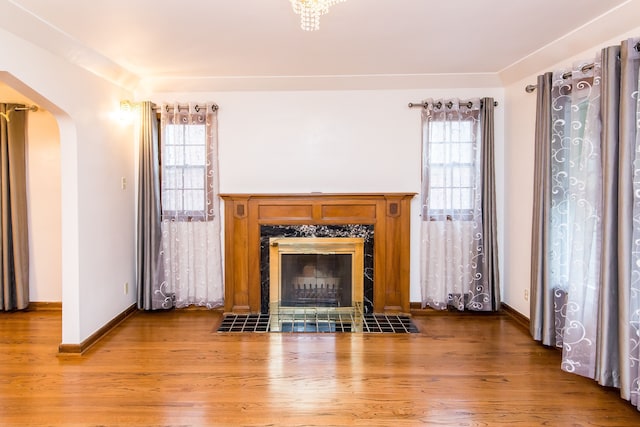 unfurnished living room featuring arched walkways, baseboards, a fireplace, and light wood-style flooring