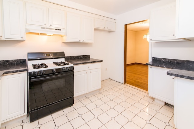 kitchen with gas range oven, dark countertops, white cabinets, light floors, and under cabinet range hood