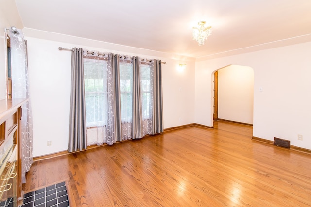 unfurnished room featuring arched walkways, baseboards, visible vents, and wood finished floors