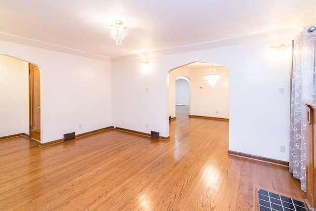 empty room featuring light wood finished floors, an inviting chandelier, visible vents, and arched walkways