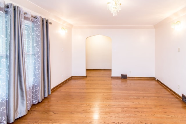 empty room with light wood finished floors, arched walkways, baseboards, and visible vents