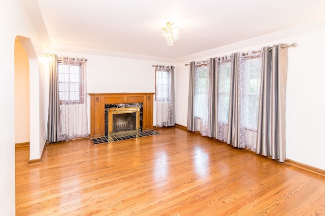 unfurnished living room featuring a fireplace, arched walkways, baseboards, and wood finished floors