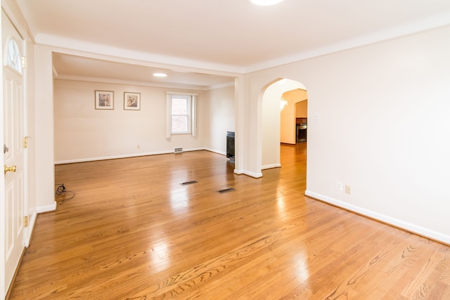 empty room with ornamental molding, light wood-style floors, baseboards, and arched walkways