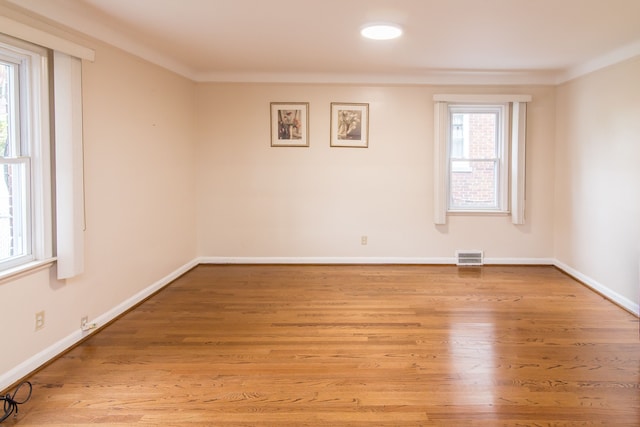 spare room with baseboards, crown molding, light wood finished floors, and visible vents