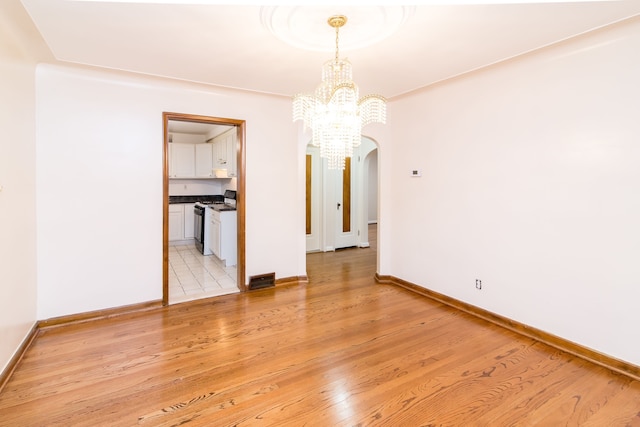 unfurnished dining area with a chandelier, light wood-style flooring, baseboards, and arched walkways