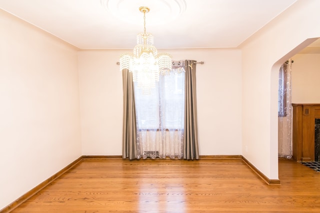 unfurnished room with a notable chandelier, baseboards, arched walkways, light wood-style floors, and a fireplace