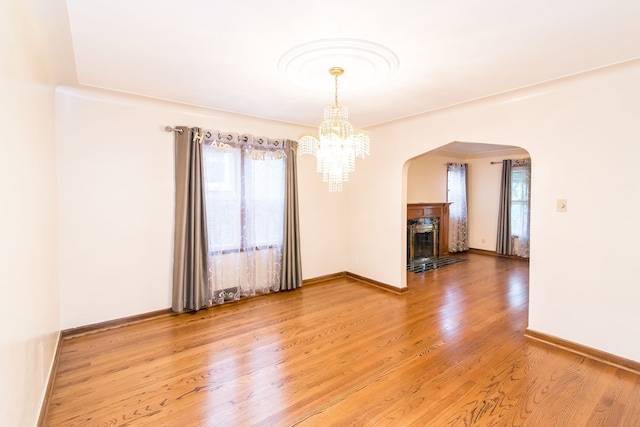 unfurnished dining area with an inviting chandelier, light wood-style flooring, arched walkways, baseboards, and a fireplace with flush hearth