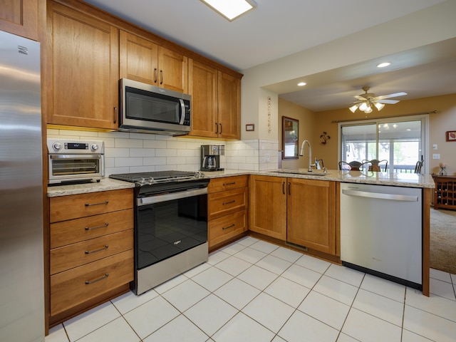 kitchen with brown cabinets, stainless steel appliances, a peninsula, and a sink