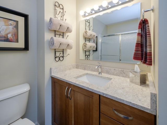 full bath featuring a shower with shower door, vanity, and toilet