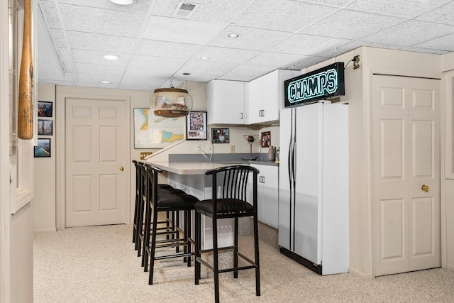 3603 Creekside Dr, Ann Arbor, MI 48105 - kitchen with a breakfast bar, freestanding refrigerator, a paneled ceiling, white cabinets, and visible vents