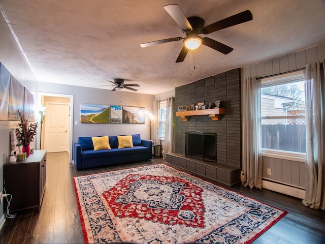 living room with wood-type flooring, a ceiling fan, a fireplace, and a baseboard radiator