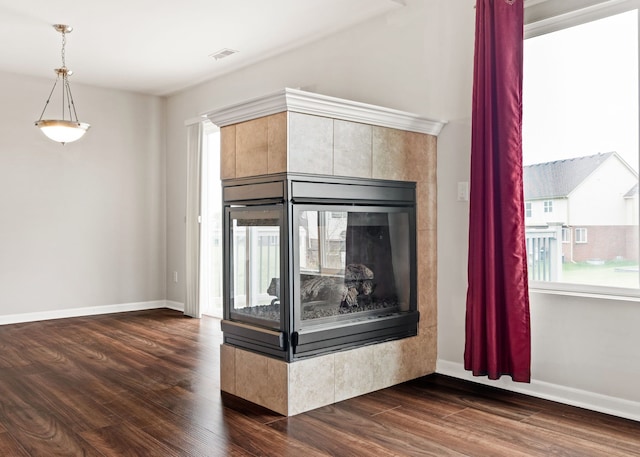room details featuring a tiled fireplace, baseboards, visible vents, and wood finished floors