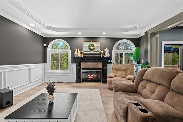living area with healthy amount of natural light, a decorative wall, a tray ceiling, crown molding, and a fireplace with flush hearth