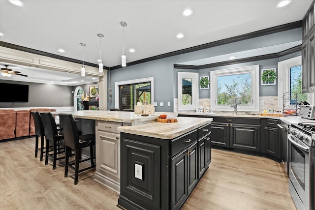 kitchen featuring a sink, ornamental molding, stainless steel gas stove, a center island, and dark cabinetry