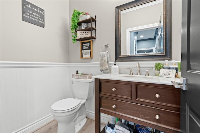 half bath with wainscoting, vanity, toilet, and wood finished floors