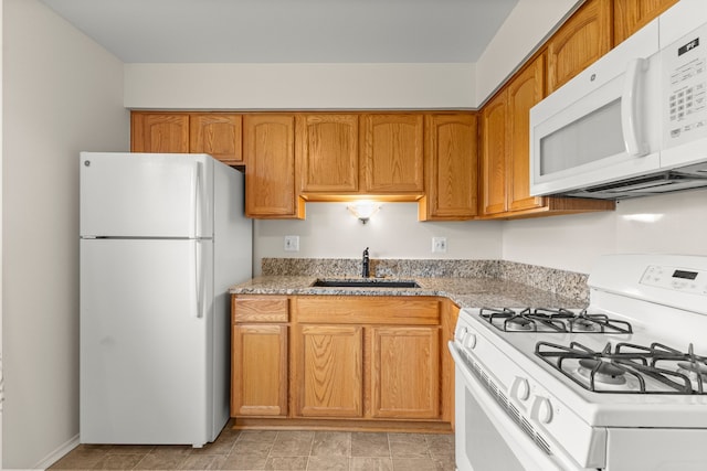 kitchen with white appliances, a sink, brown cabinets, and light stone counters