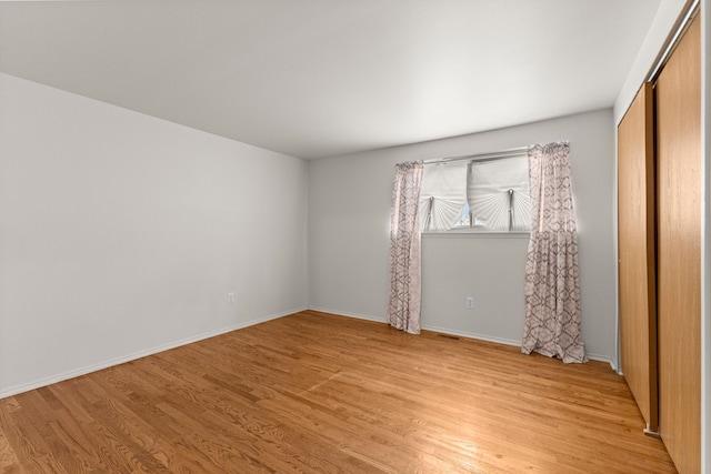 unfurnished bedroom featuring light wood-style flooring, baseboards, and a closet