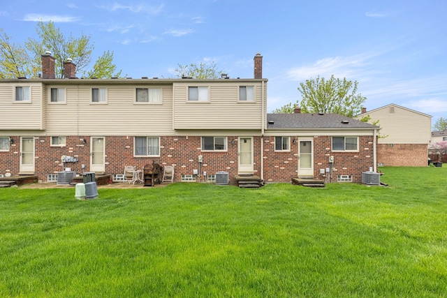 back of property with entry steps, a chimney, cooling unit, brick siding, and a yard