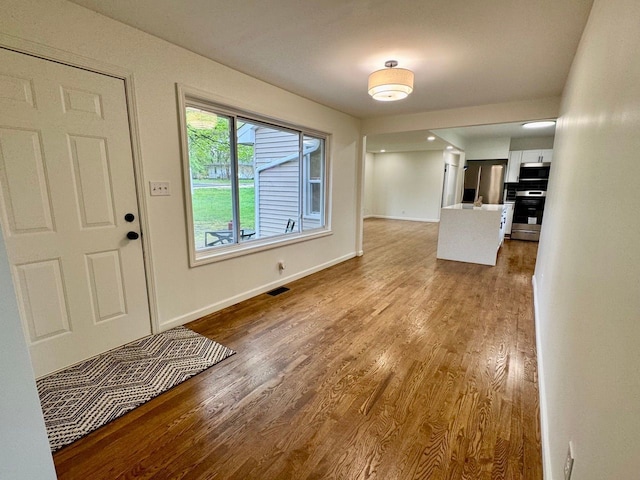 foyer entrance with baseboards, visible vents, and wood finished floors