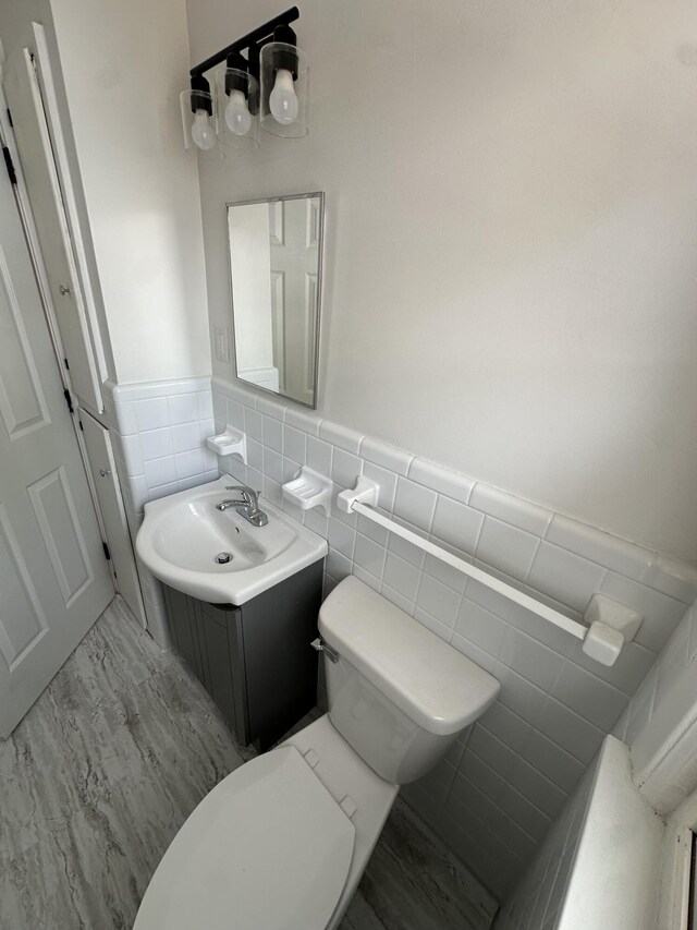 bathroom featuring tile walls, toilet, vanity, and a wainscoted wall
