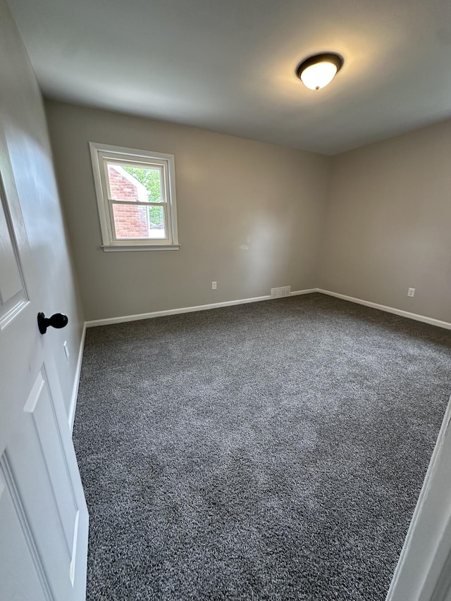 spare room with visible vents, baseboards, and dark colored carpet