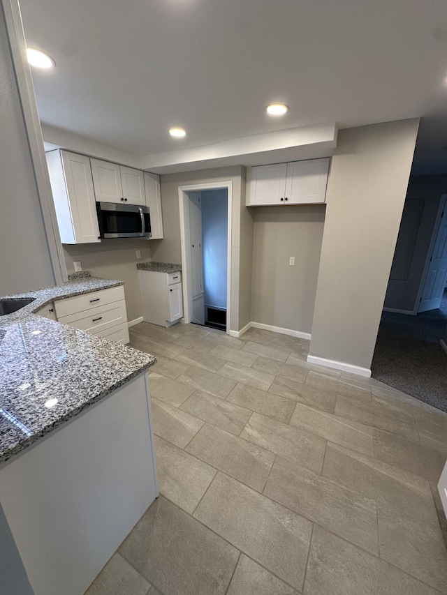 kitchen featuring white cabinetry, baseboards, stainless steel microwave, and light stone countertops