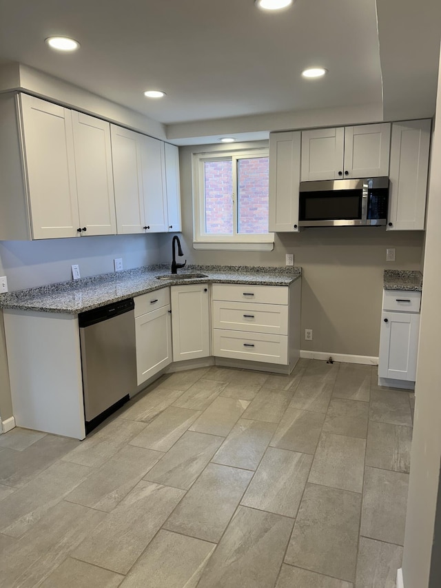 kitchen featuring recessed lighting, baseboards, light stone counters, a sink, and appliances with stainless steel finishes