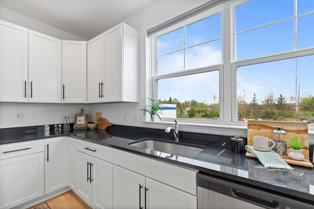 kitchen with a sink, stainless steel dishwasher, dark stone counters, and white cabinetry