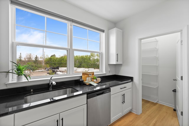 kitchen with dishwasher, a sink, light wood-style floors, white cabinets, and dark stone counters