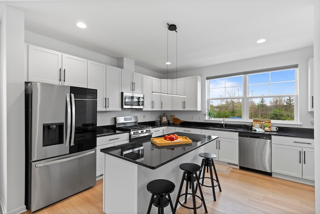 kitchen featuring appliances with stainless steel finishes, a kitchen breakfast bar, dark countertops, light wood finished floors, and recessed lighting