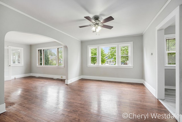 empty room with wood finished floors, baseboards, ornamental molding, and arched walkways