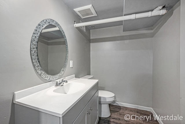 half bath featuring toilet, vanity, visible vents, and wood finished floors