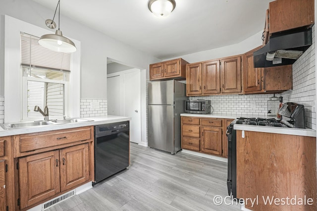 kitchen with a sink, brown cabinetry, visible vents, black appliances, and decorative backsplash