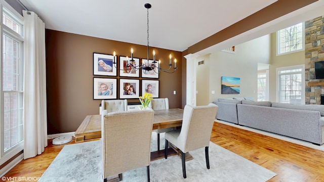 7272 Holden Rd, Stevensville, MI 49127 - dining room featuring a stone fireplace, a notable chandelier, light wood-style flooring, and visible vents