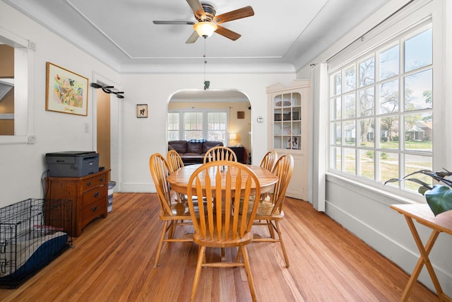 dining area with light wood-style flooring, arched walkways, and a ceiling fan