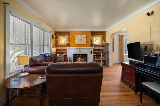 living area with crown molding, light wood-style flooring, arched walkways, and a healthy amount of sunlight