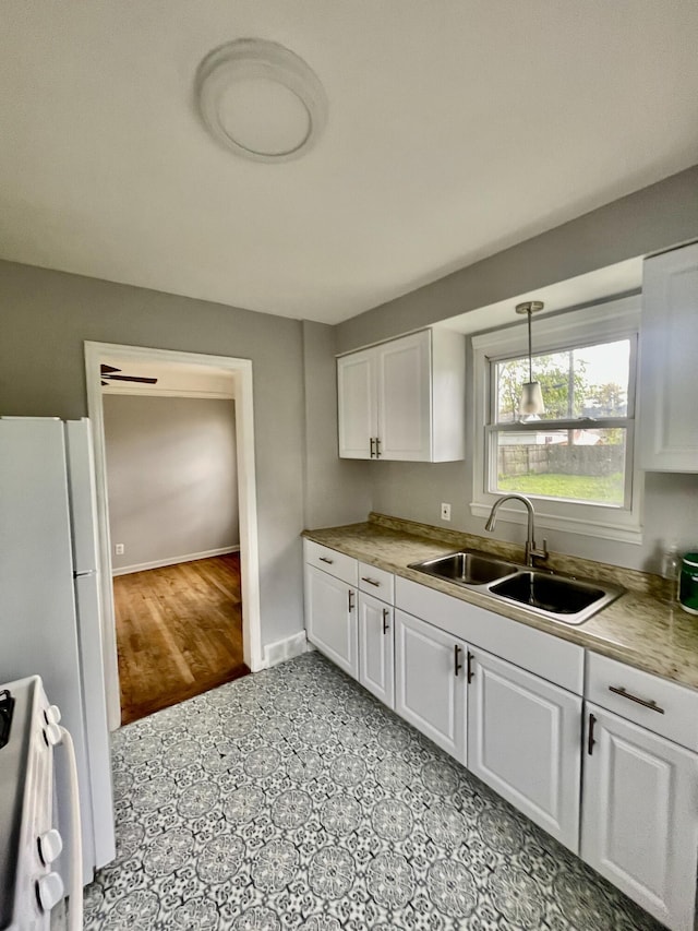 kitchen featuring a sink, stove, white cabinetry, freestanding refrigerator, and baseboards