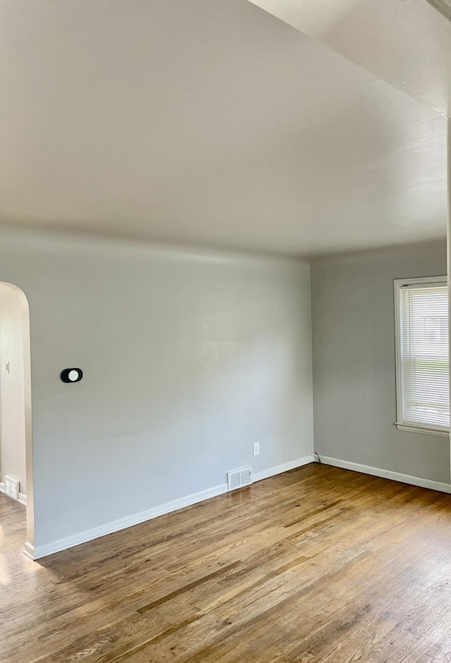 unfurnished room with arched walkways, wood finished floors, and baseboards