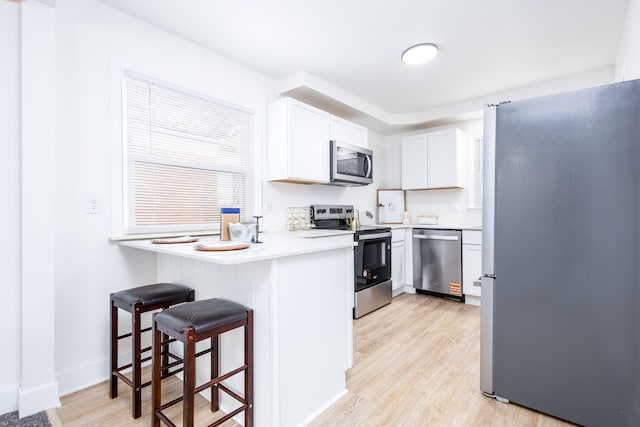 21430 Ridgedale St, Oak Park, MI 48237 - kitchen with a peninsula, appliances with stainless steel finishes, a kitchen breakfast bar, white cabinetry, and light wood-style floors