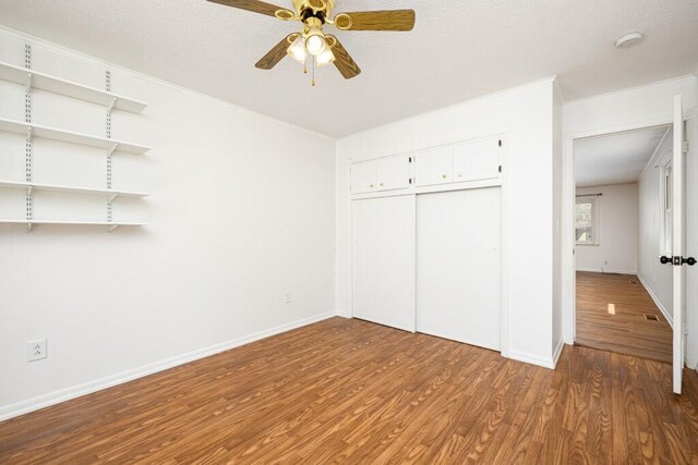 unfurnished bedroom with wood finished floors, a closet, crown molding, baseboards, and ceiling fan