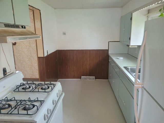 kitchen featuring white appliances, a wainscoted wall, wooden walls, under cabinet range hood, and light countertops