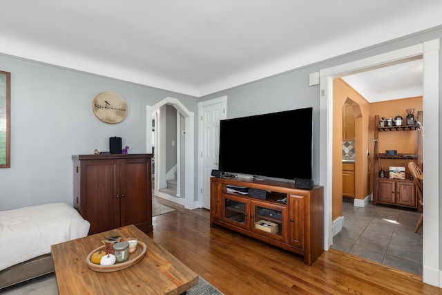 living room with arched walkways, stairs, wood finished floors, and baseboards