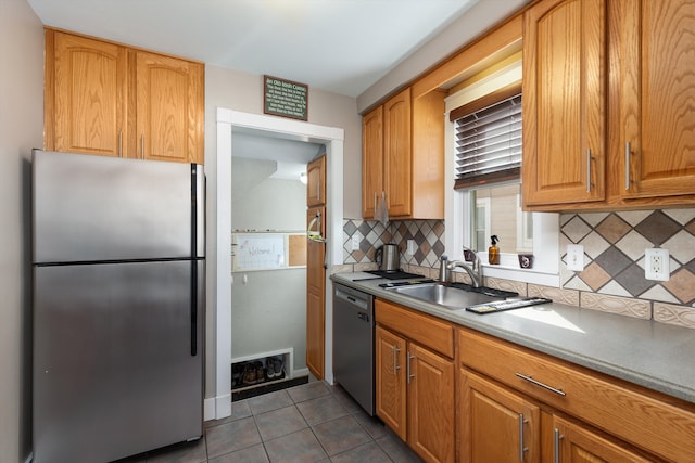 kitchen with stainless steel appliances, a sink, decorative backsplash, tile patterned floors, and brown cabinets
