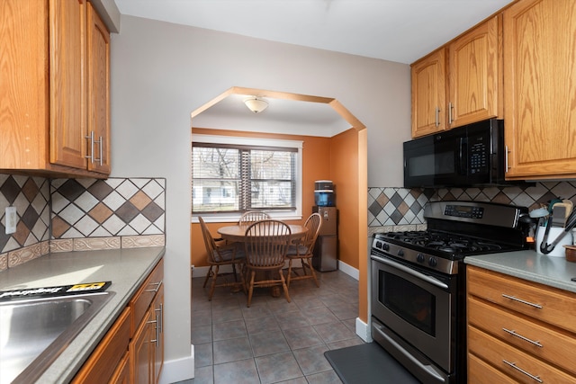 kitchen featuring stainless steel range with gas cooktop, black microwave, tile patterned flooring, and baseboards