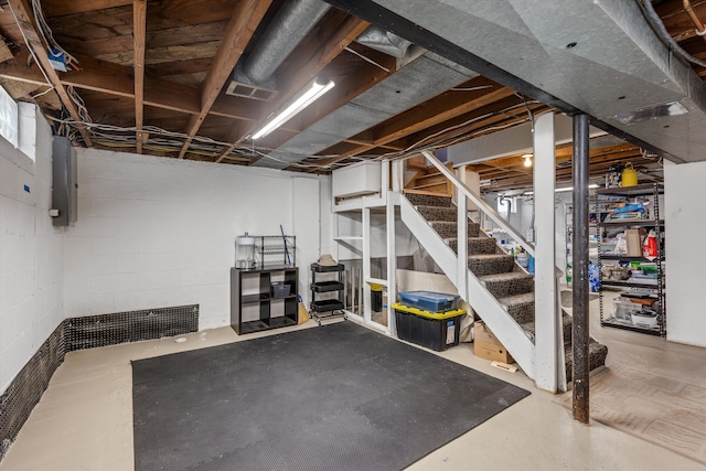 unfinished basement featuring electric panel, visible vents, concrete block wall, and stairway